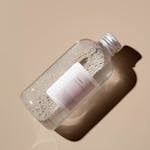 A close-up of a glass bottle filled with tonic water on a beige surface.