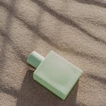 Elegant green perfume bottle resting on textured sand, evoking a serene and natural aesthetic.