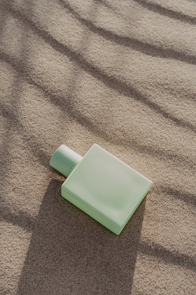 Elegant green perfume bottle resting on textured sand, evoking a serene and natural aesthetic.
