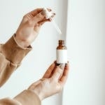 A close-up of hands holding a skincare dropper bottle with a beige sweater and blank label.