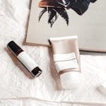 Flat lay of skincare products on textured paper with an open magazine, showcasing a stylish aesthetic.